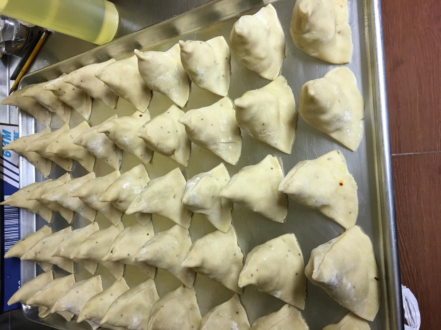 Tray of hand-folded samosas ready for the fryer